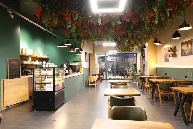 Kafe bölümü: yeşil bar, sarmaşıklı tavan ve ahşap masalar