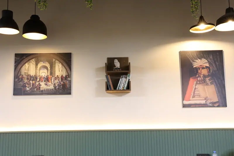 Duvarda tablolar, küçük kitap rafı ve sarkıt lambalar